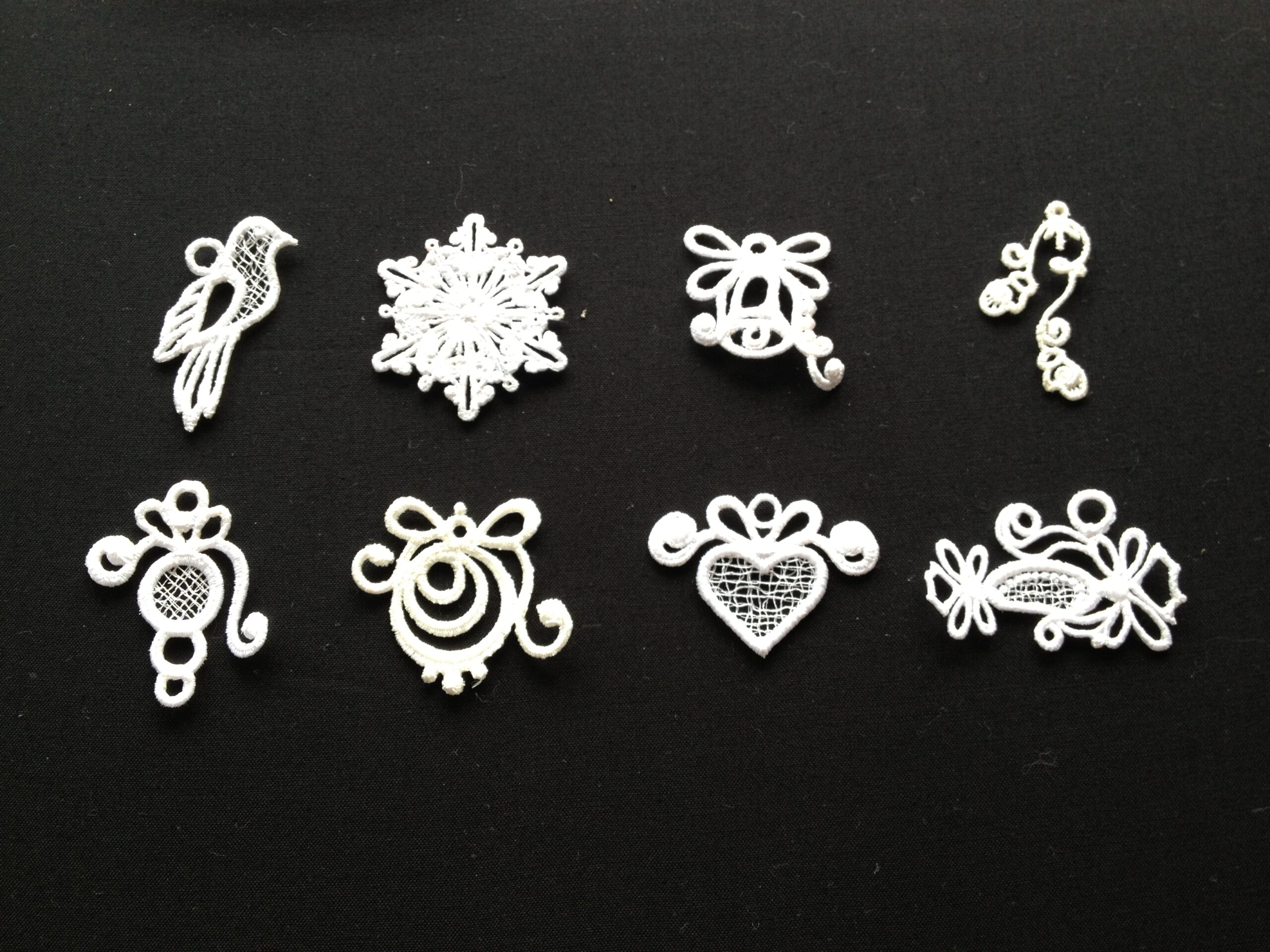 An embroidery design of intricate white motifs including a bird, a snowflake, and various decorative shapes and bows.
