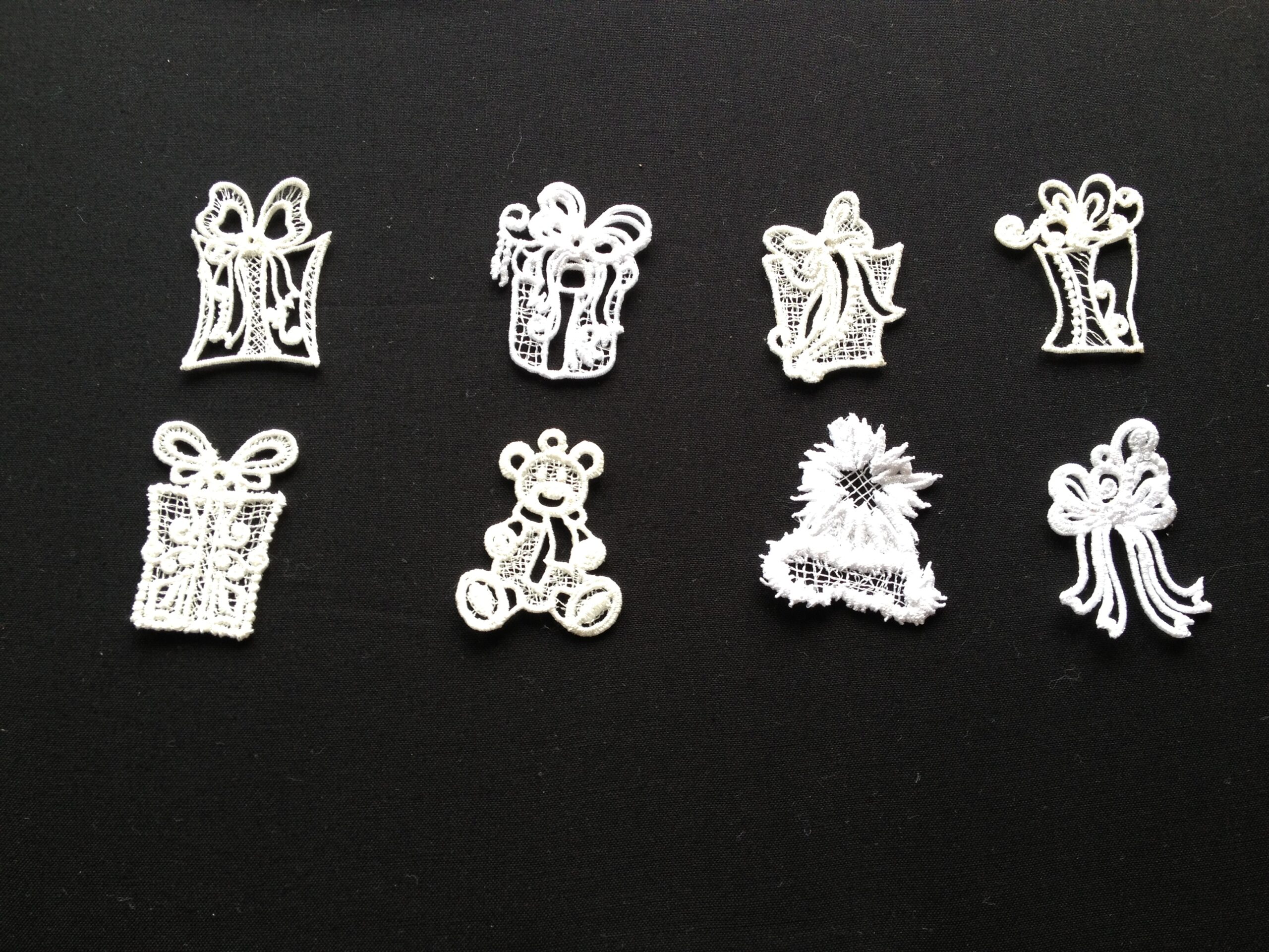 An embroidery design of various festive motifs including gifts, a teddy bear, and decorative bows in intricate white detailing.