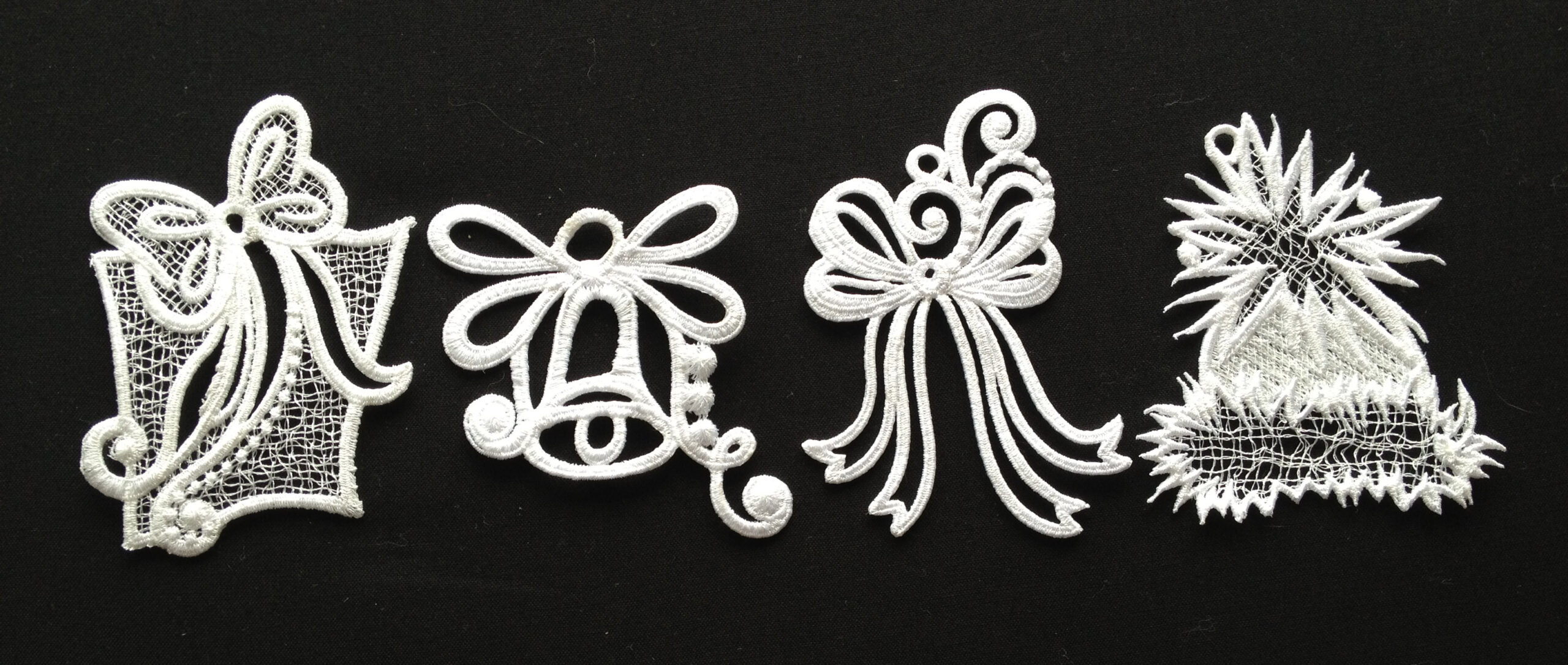 An embroidery design of four festive white elements including a gift, a bell, a bow, and a decorative hat, showcasing intricate lace patterns.
