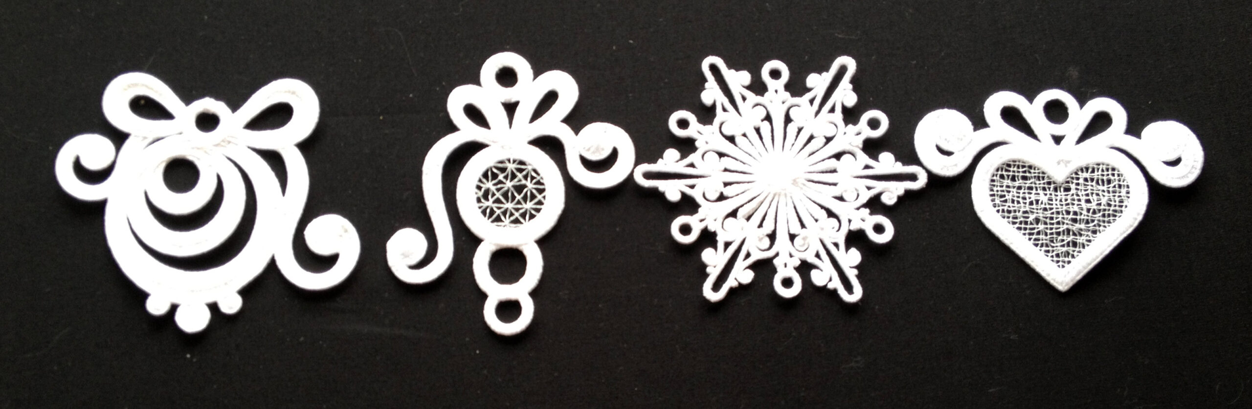 An embroidery design of four intricate white lace motifs, including a bow, a circular shape, a snowflake, and a heart, each featuring delicate patterns.