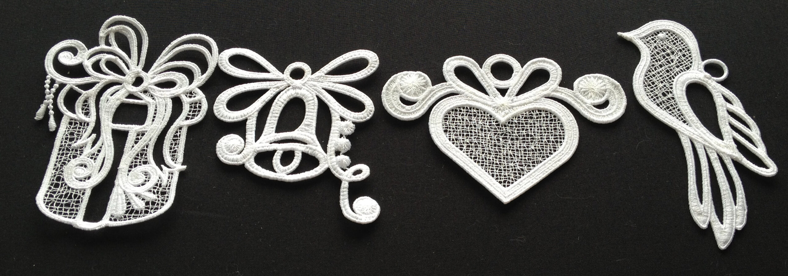 An embroidery design of four intricate white lace motifs, including a gift box with a bow, a bell, a heart, and a bird, showcasing delicate patterns.
