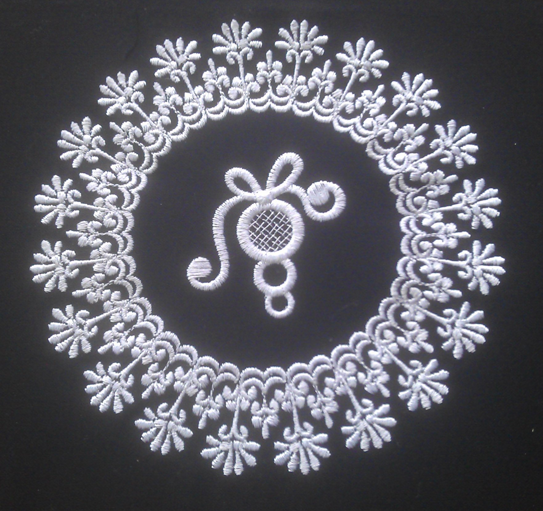 An embroidery design of a circular lace pattern featuring intricate floral motifs and a central decorative element resembling a bow.