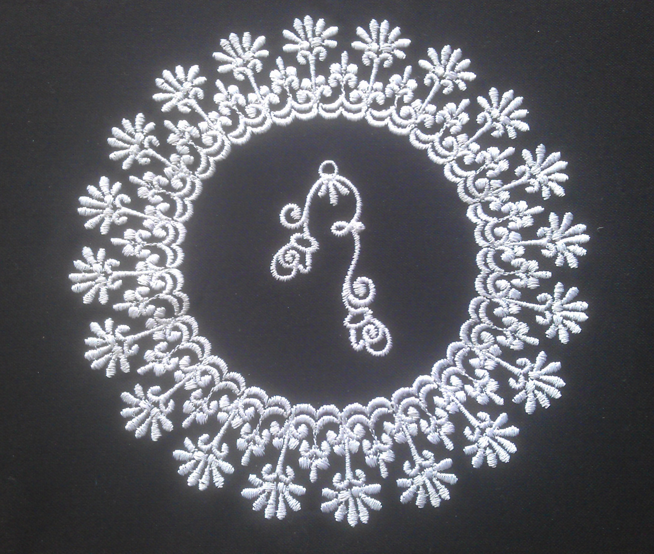 An embroidery design of a circular arrangement of delicate floral motifs surrounding a central ornate element.