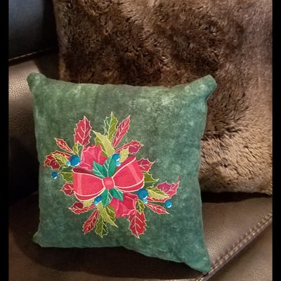 An embroidery design of a festive red bow surrounded by green holly leaves and blue accents.