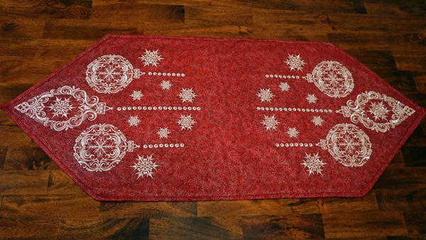An embroidery design of intricate white ornaments and snowflakes on a rich red background.
