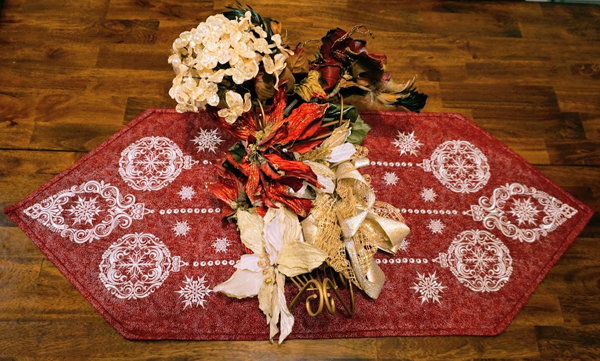 An embroidery design of intricate ornaments and snowflakes in white, beautifully set against a rich red background.