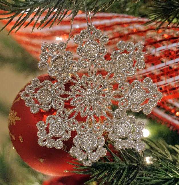 An embroidery design of a delicate silver snowflake with intricate details and a symmetrical pattern.