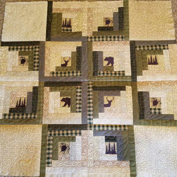 An embroidery design of a quilt featuring a patchwork arrangement with silhouettes of bears and moose, surrounded by earthy tones and checkered patterns.