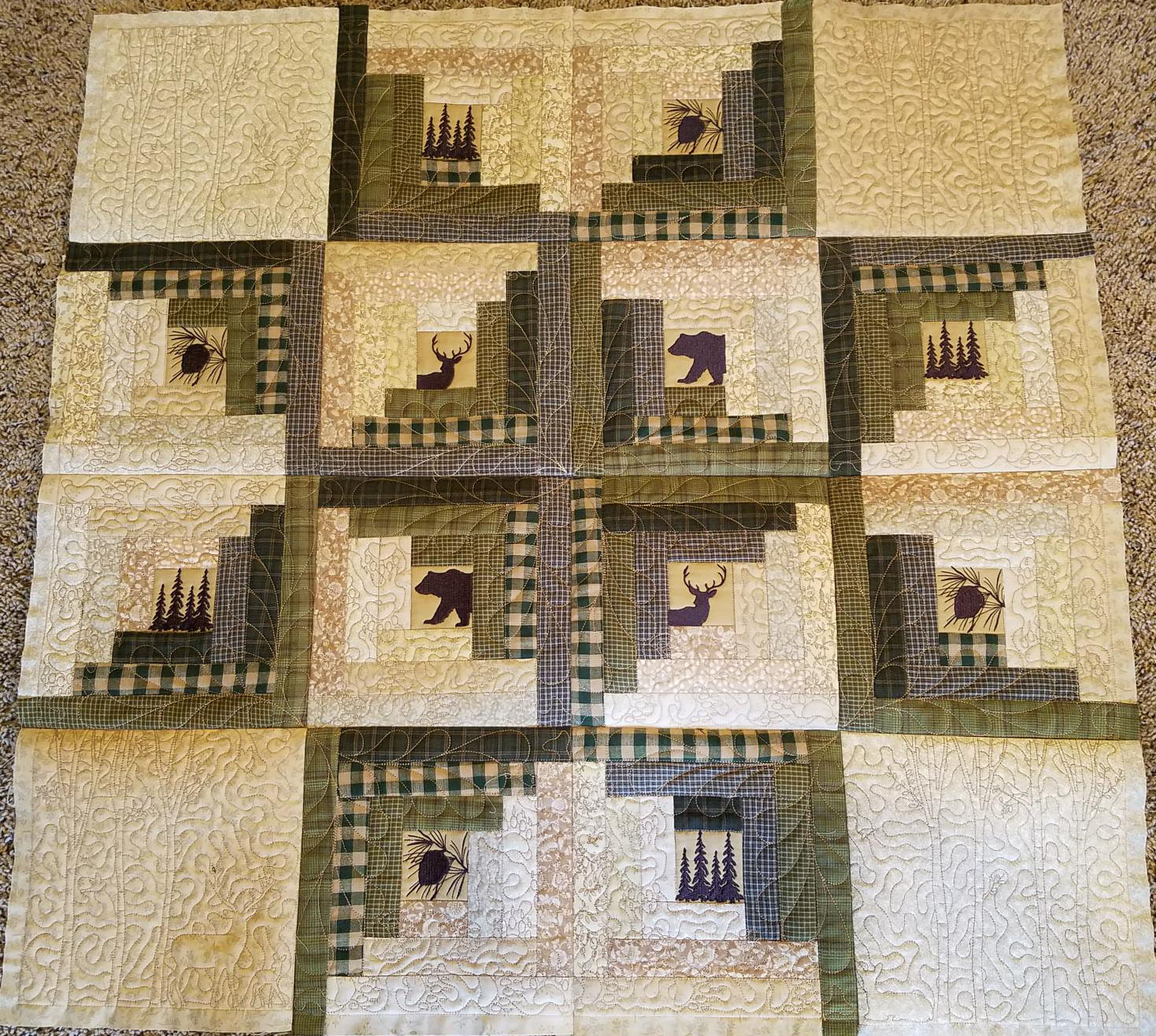 IntoTheWoods An embroidery design of a quilt featuring a patchwork arrangement with silhouettes of bears and moose, surrounded by earthy tones and checkered patterns.