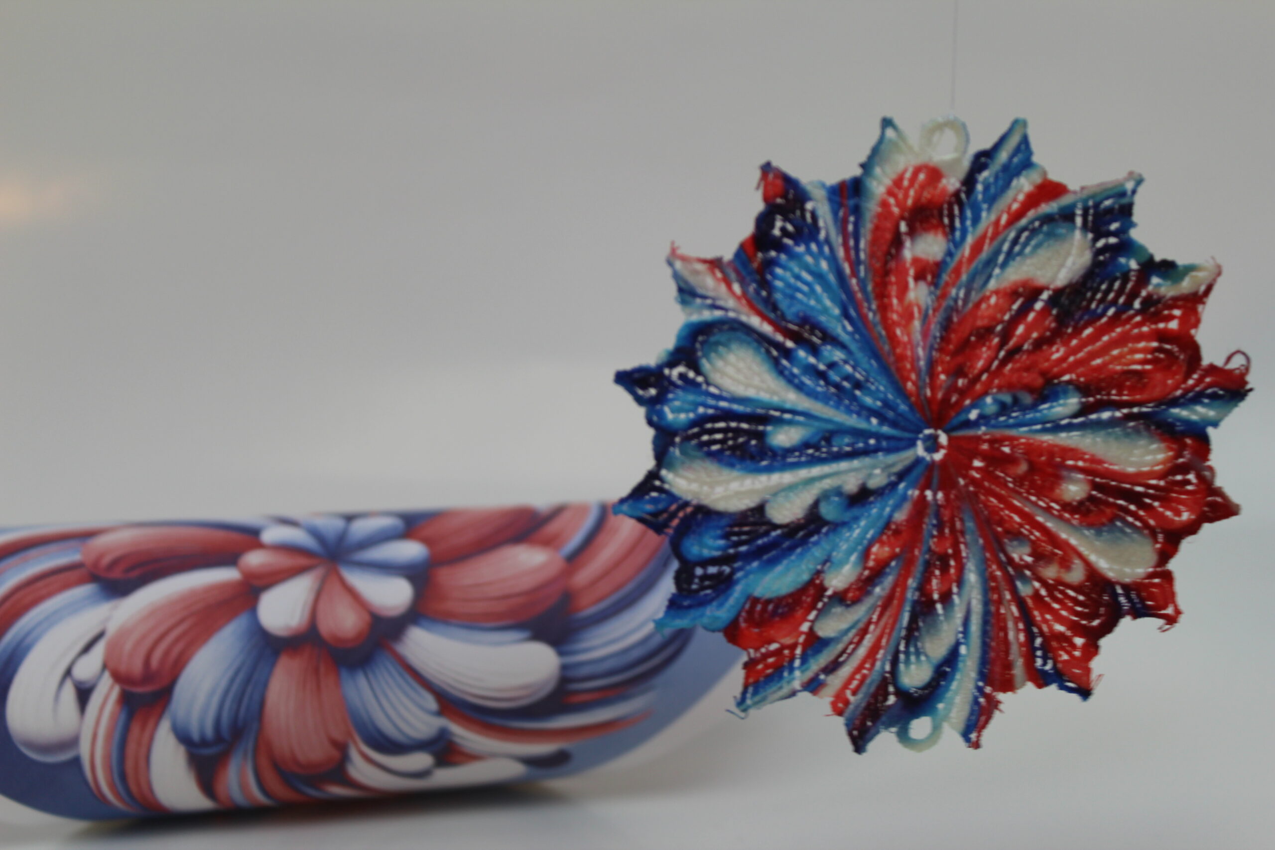 An embroidery design of a vibrant, layered flower motif in red, blue, and white threads, showcasing intricate detailing and texture.
