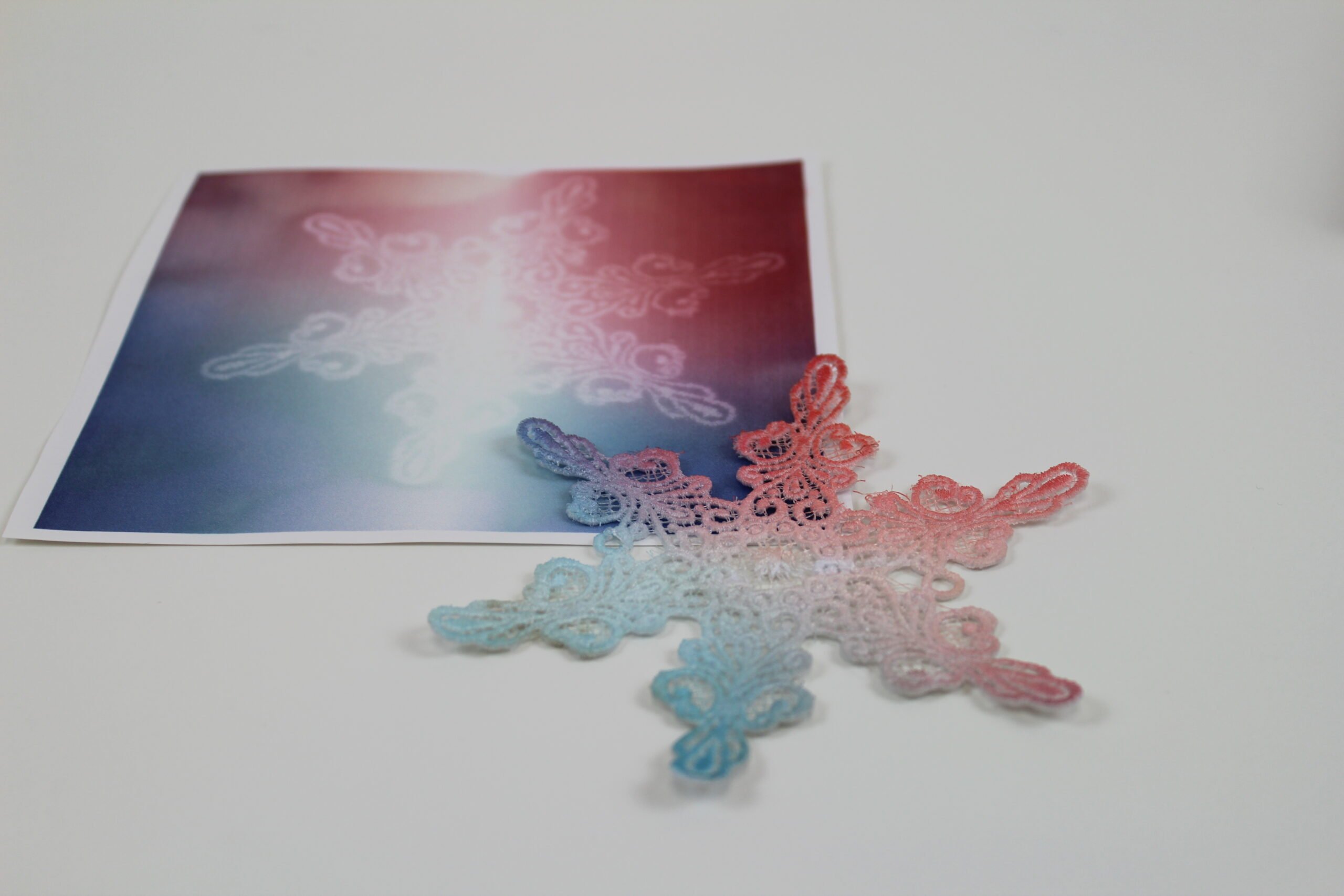 An embroidery design of a delicate snowflake featuring intricate patterns and a gradient of soft colors transitioning from blue to pink.