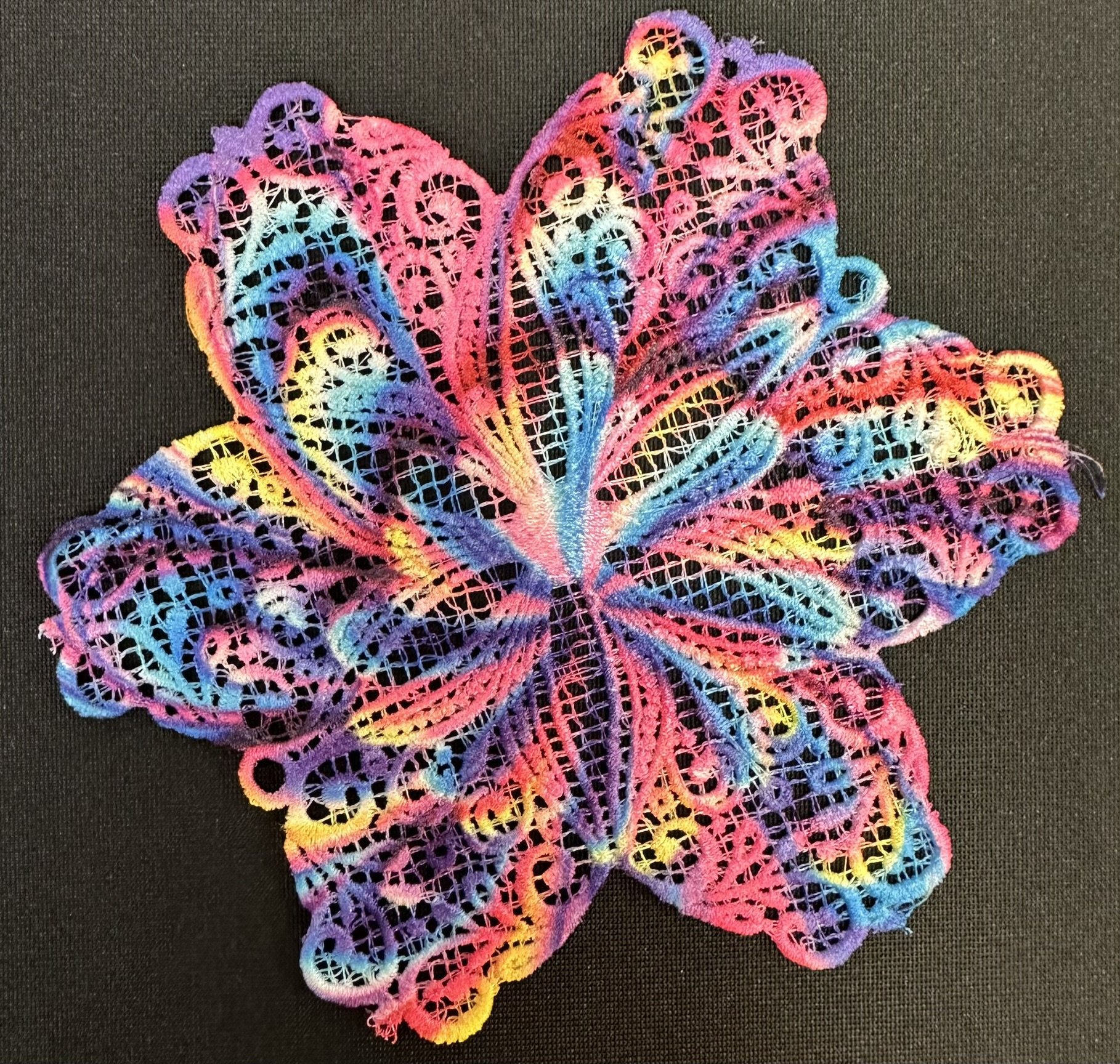 An embroidery design of a vibrant, multicolored flower with intricate lace-like detailing.