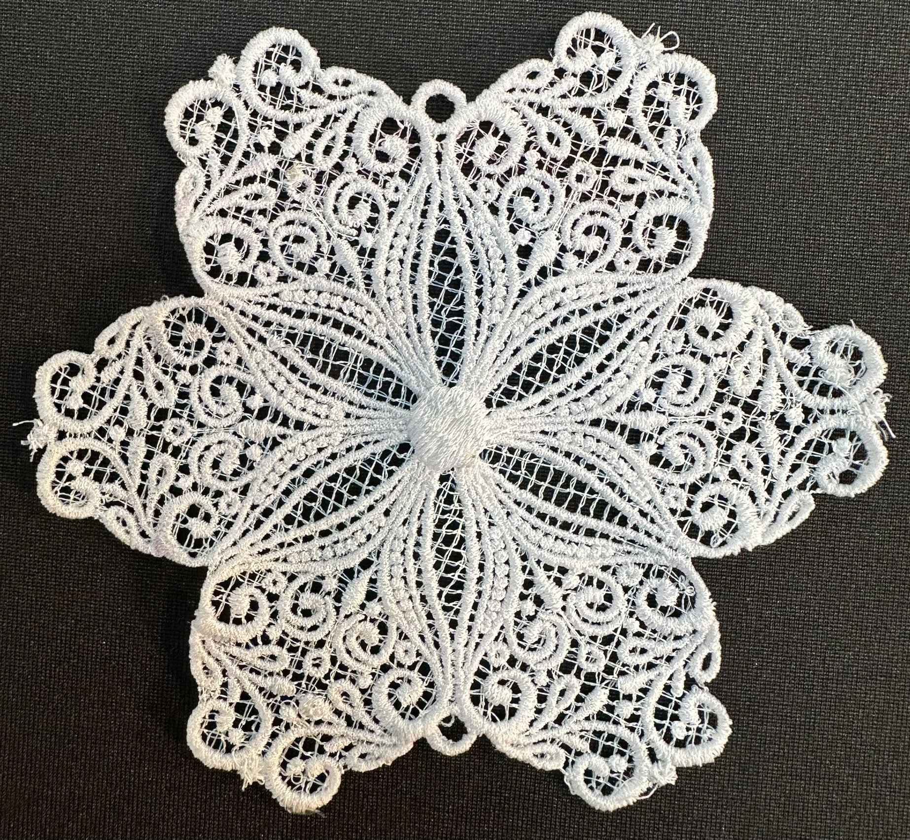 An embroidery design of an intricate floral lace pattern featuring elegant swirls and a central motif.