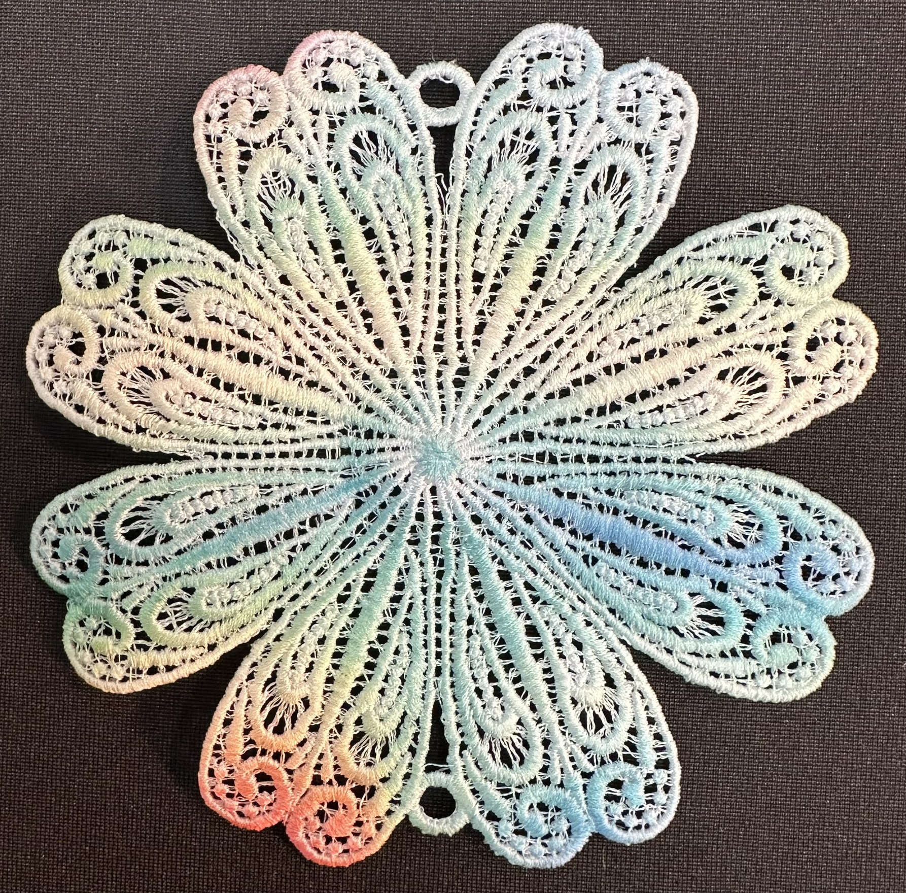 An embroidery design of a delicate, multicolored floral motif featuring intricate swirling patterns.