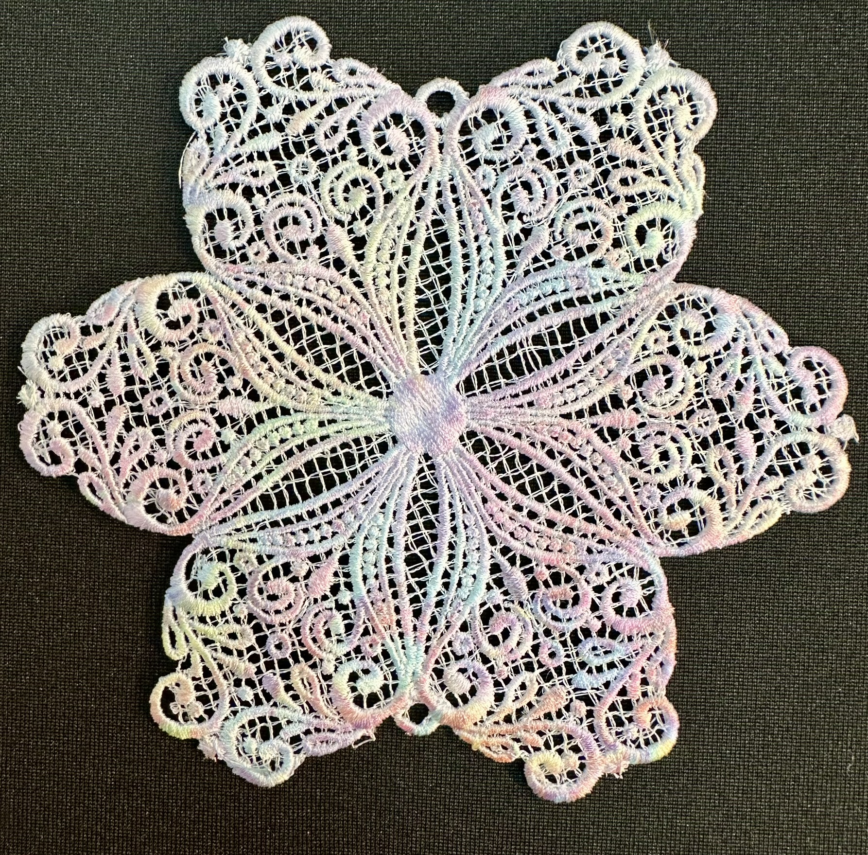 An embroidery design of a delicate, pastel-colored floral motif featuring intricate swirls and lace-like detailing.