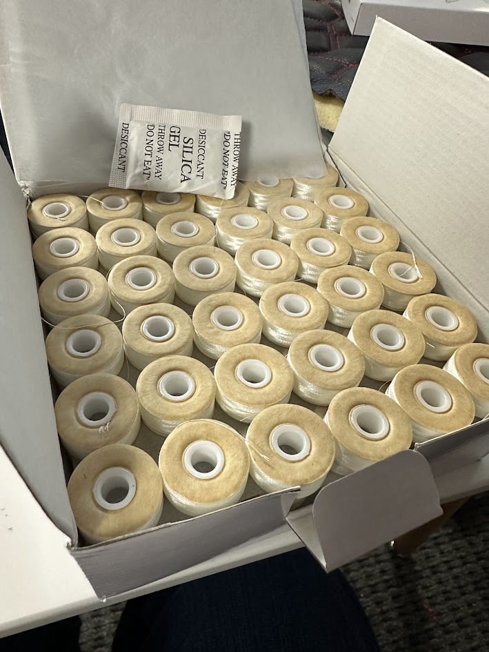 An embroidery design of a neatly organized box filled with multiple spools of thread.