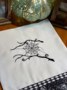 An embroidery design of an intricate black spider web with decorative swirls and tendrils.