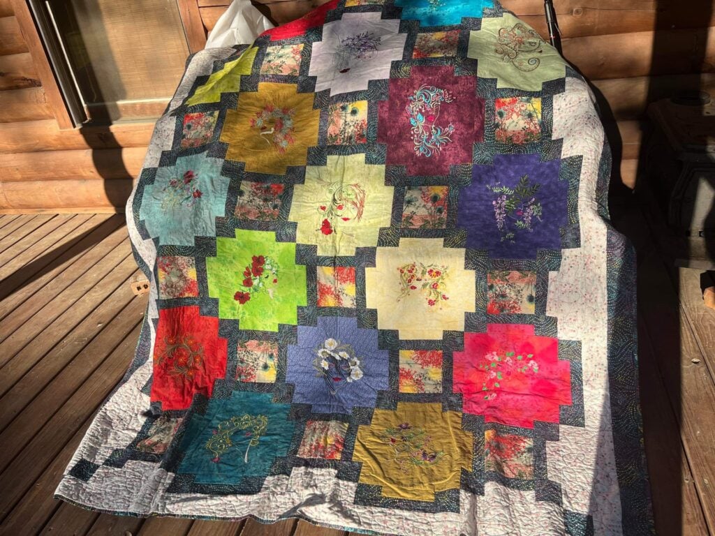 An embroidery design of colorful floral patterns arranged in geometric blocks on a quilt backdrop.