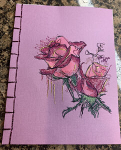 An embroidery design of delicate pink roses with intricate details and hints of green foliage.