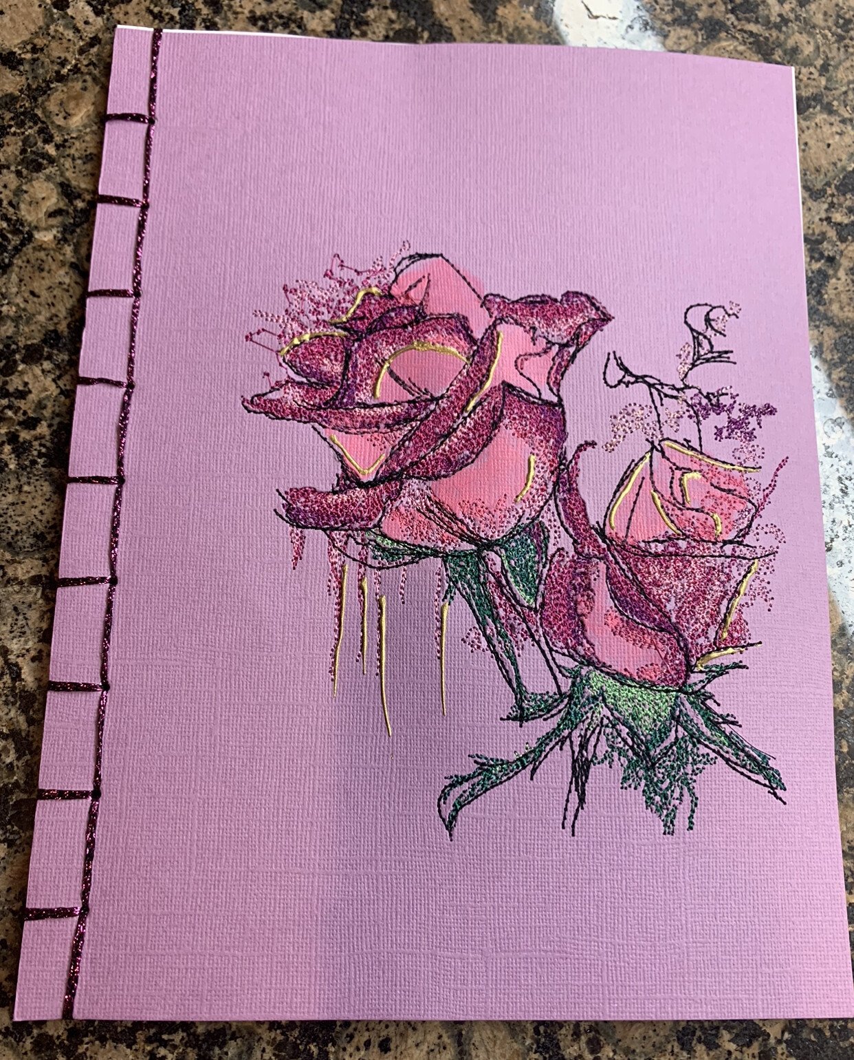 An embroidery design of delicate pink roses with intricate details and hints of green foliage.